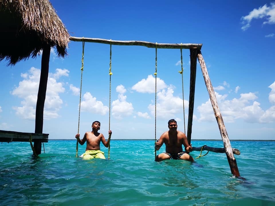 Two guests relaxing on wooden swings set over the turquoise lagoon at Bacalar