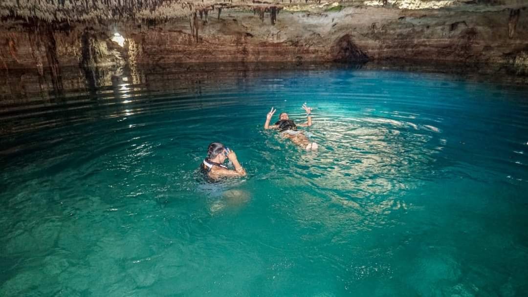 Two guests swimming in a crystal-clear underground cenote with stalactites