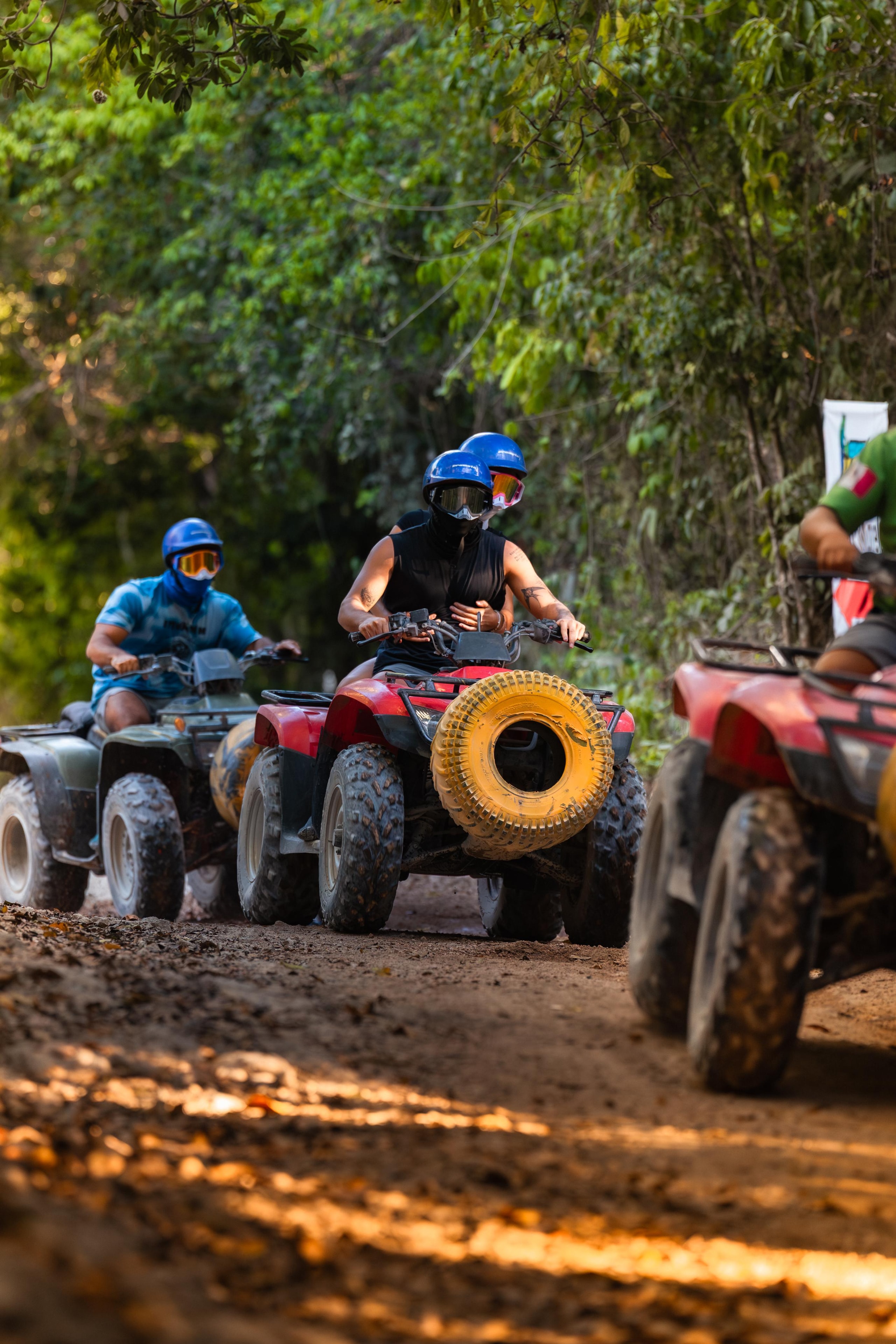 Three riders on ATVs speeding through a jungle dirt trail in Cancun
