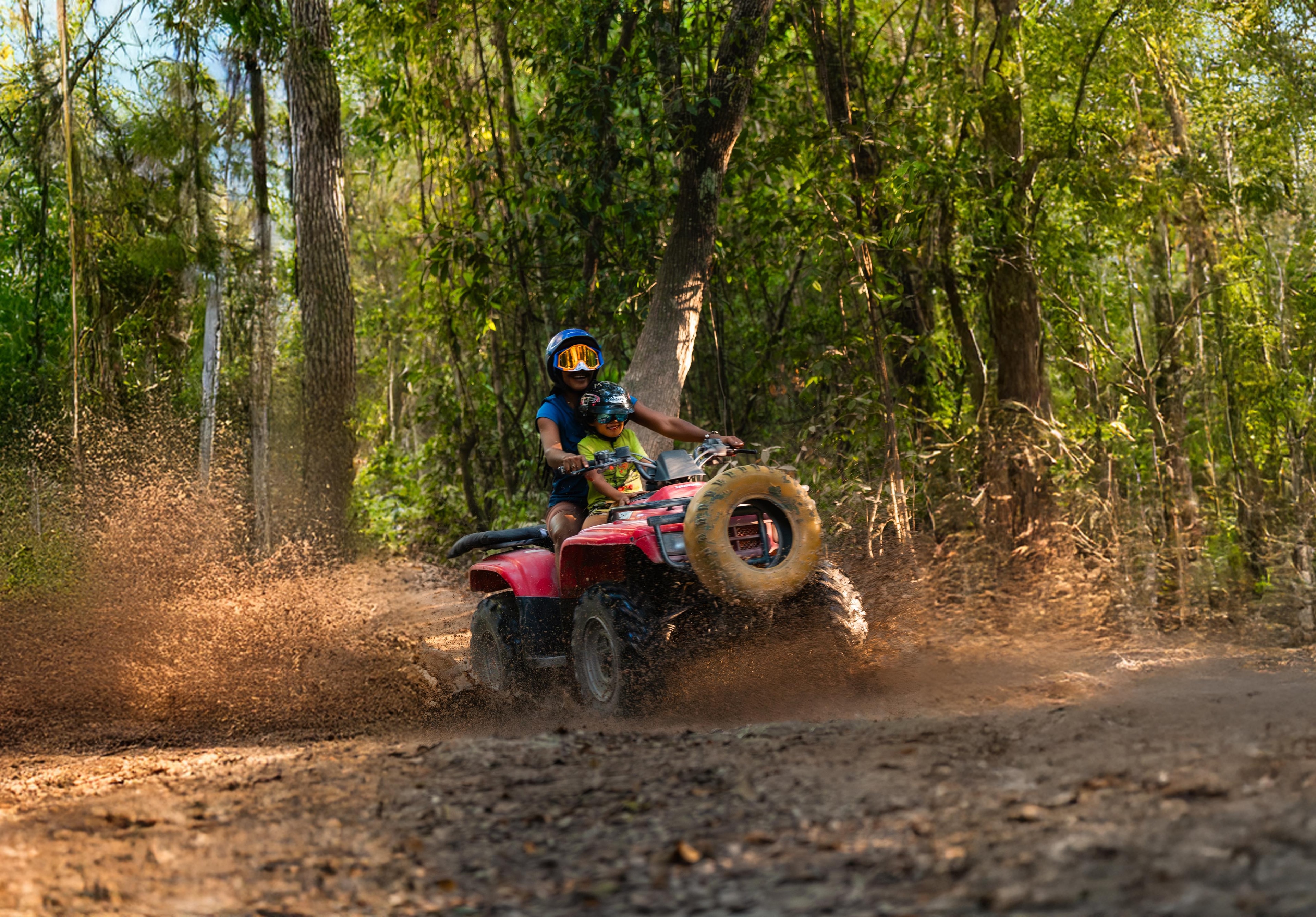 Parent and child riding an ATV together through the jungle trail