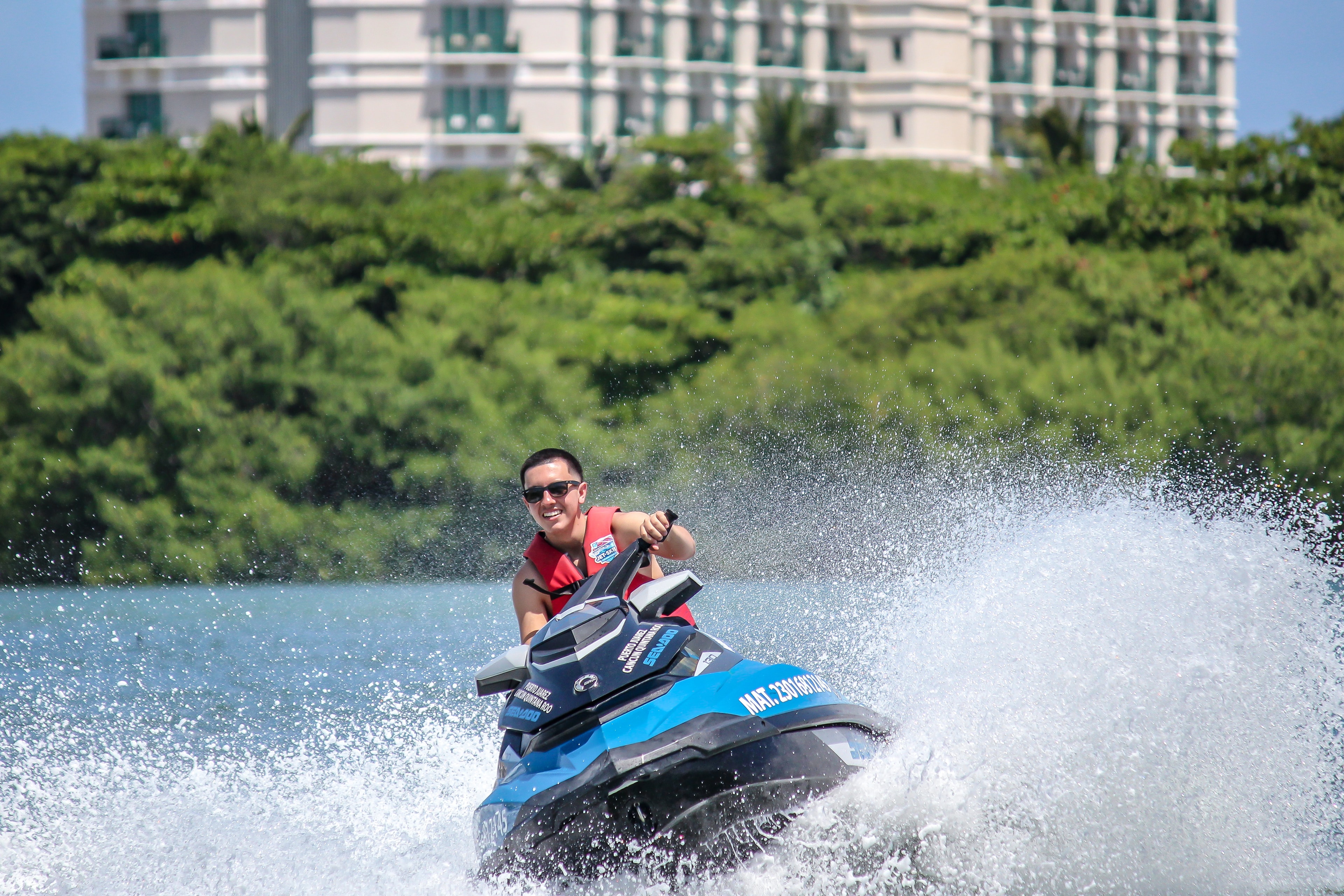 Rider on a jet ski sending up a huge spray of water with Cancun Hotel Zone skyline behind