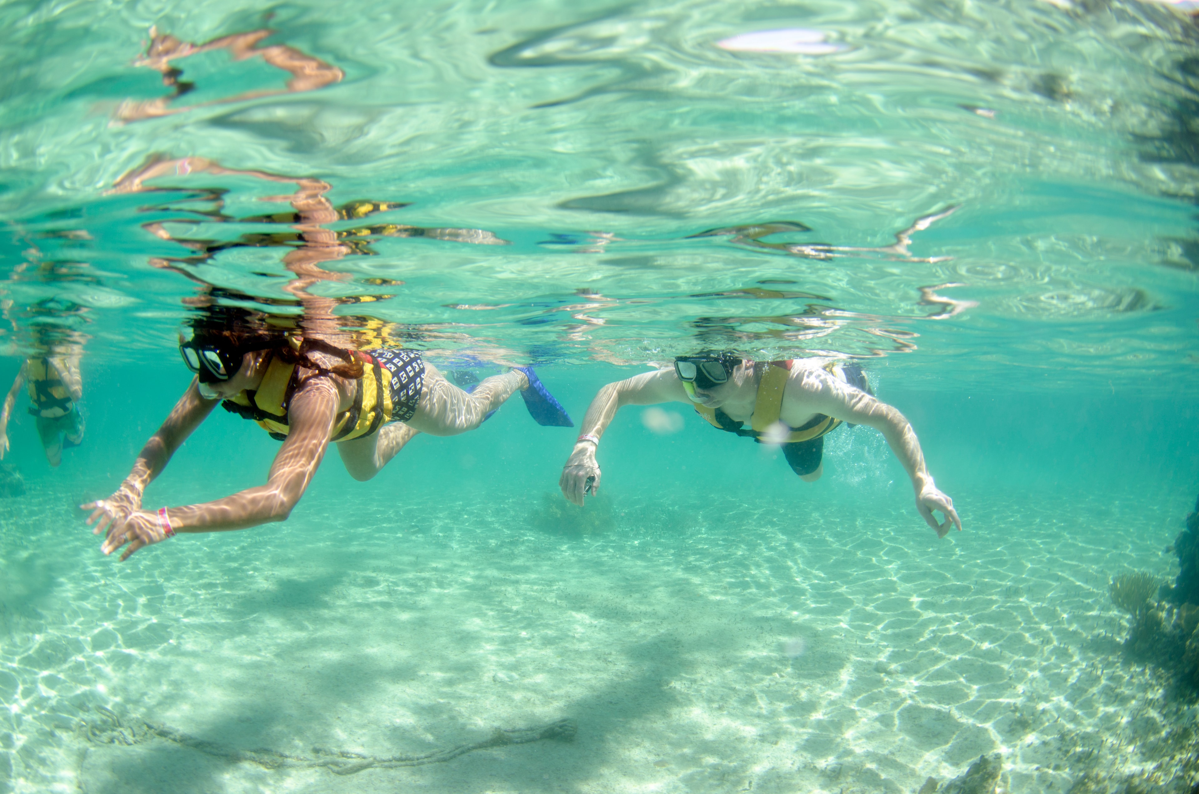 Two snorkelers gliding through crystal-clear turquoise water wearing masks and life jackets in Cancun