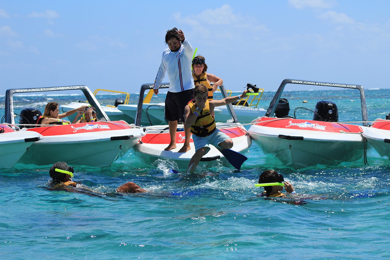 Boy jumping off a Jungle Tour speedboat into turquoise Caribbean water as snorkelers swim below