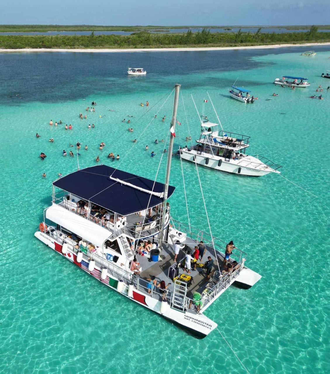 Aerial view of the Morningstar catamaran anchored in crystal-clear turquoise waters off Cozumel with snorkellers swimming around it