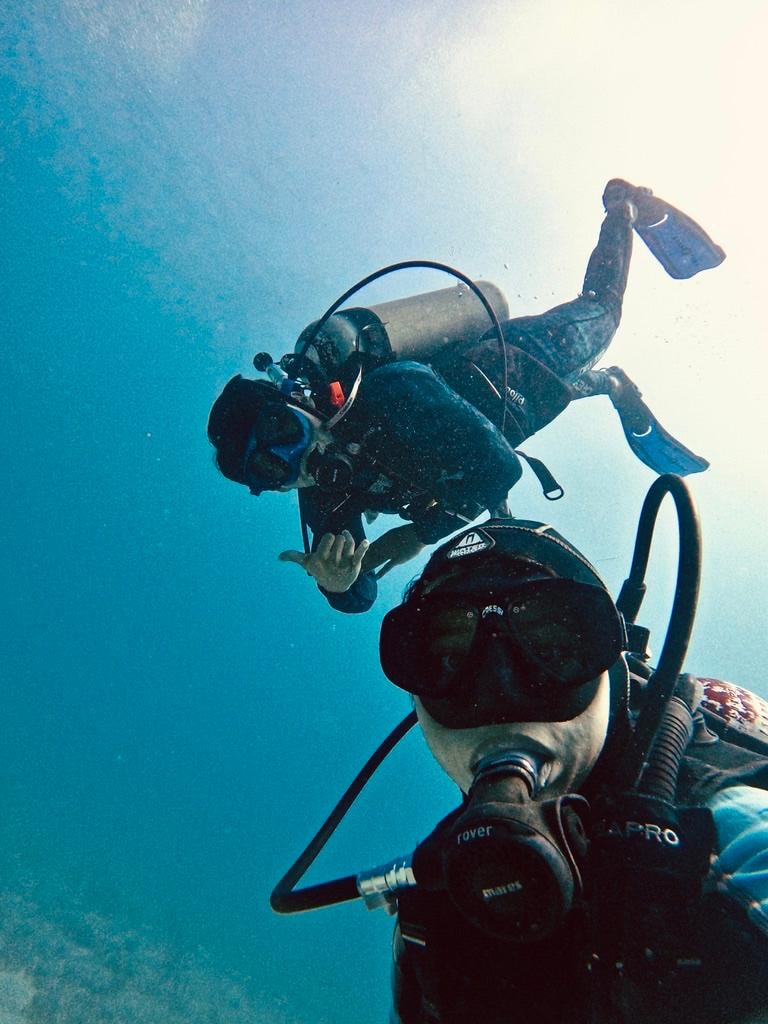 Two scuba divers taking an underwater selfie in the bright blue waters of the Cozumel reef